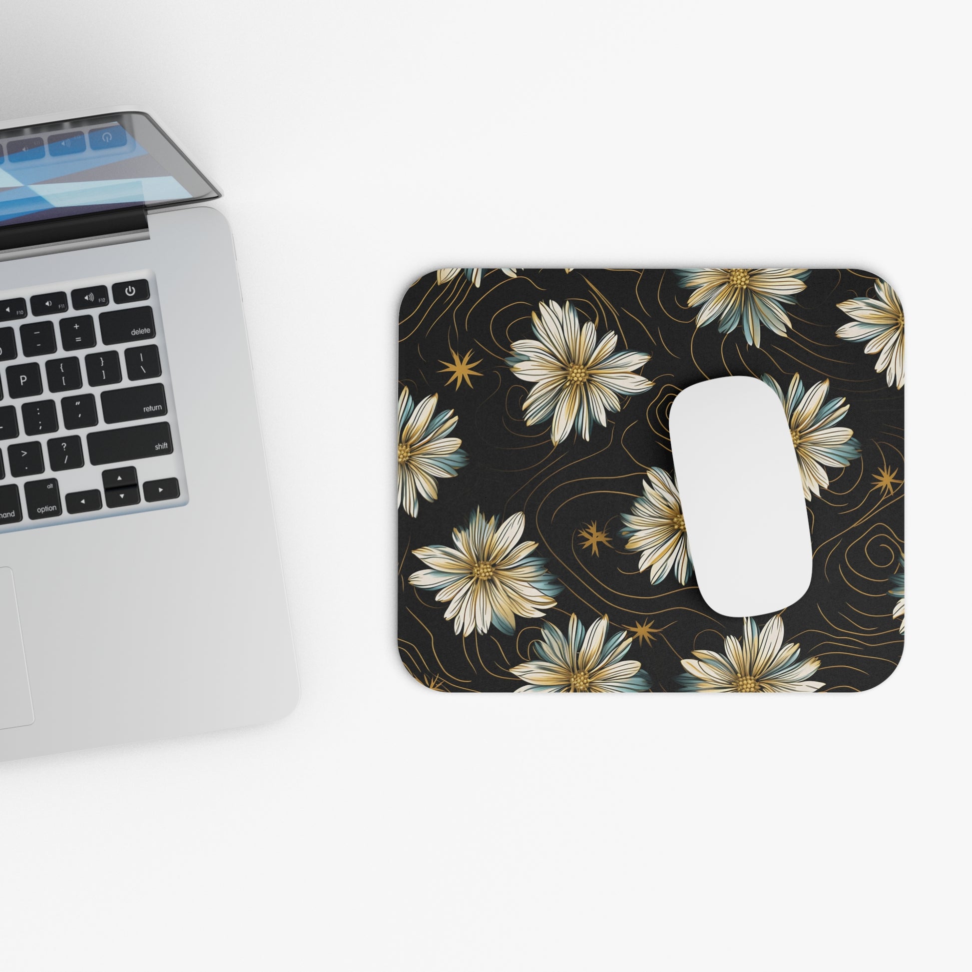Mousepad with black background and floral daisy pattern, next to a laptop.