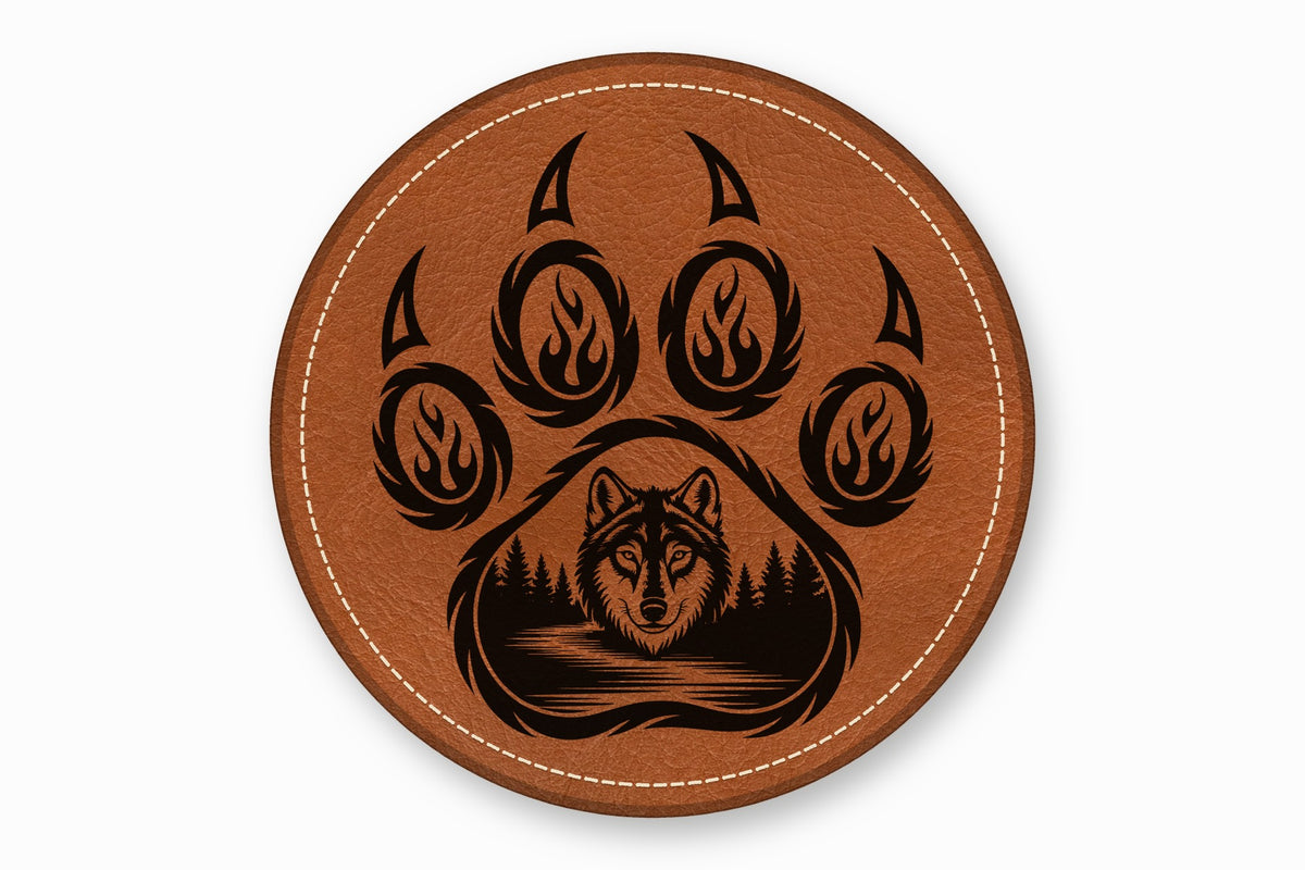 Round brown leather coaster with white stitched edge, featuring a black engraved bear paw and wolf forest scene.