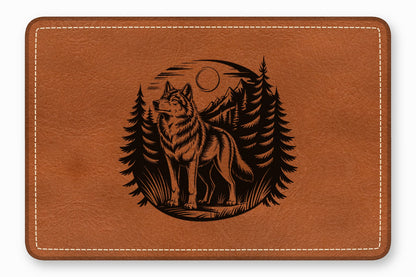 Brown leather rectangle with rounded corners, featuring an engraved graphic of a wolf in a forest.