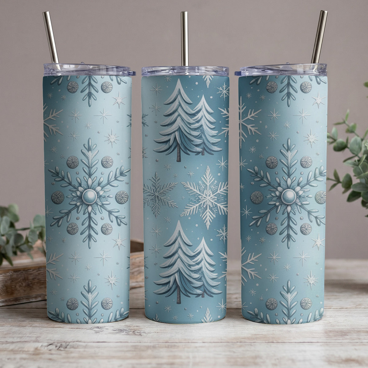 Three blue tumblers with snow and Christmas tree patterns, each with a silver straw.