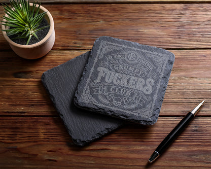 Slate coasters engraved with "Est. Since Forever Grumpy Fuckers Club" and decorative elements.