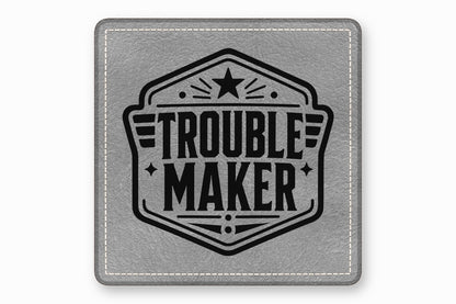 Square grey leather patch with white stitched border featuring a black Trouble Maker emblem.