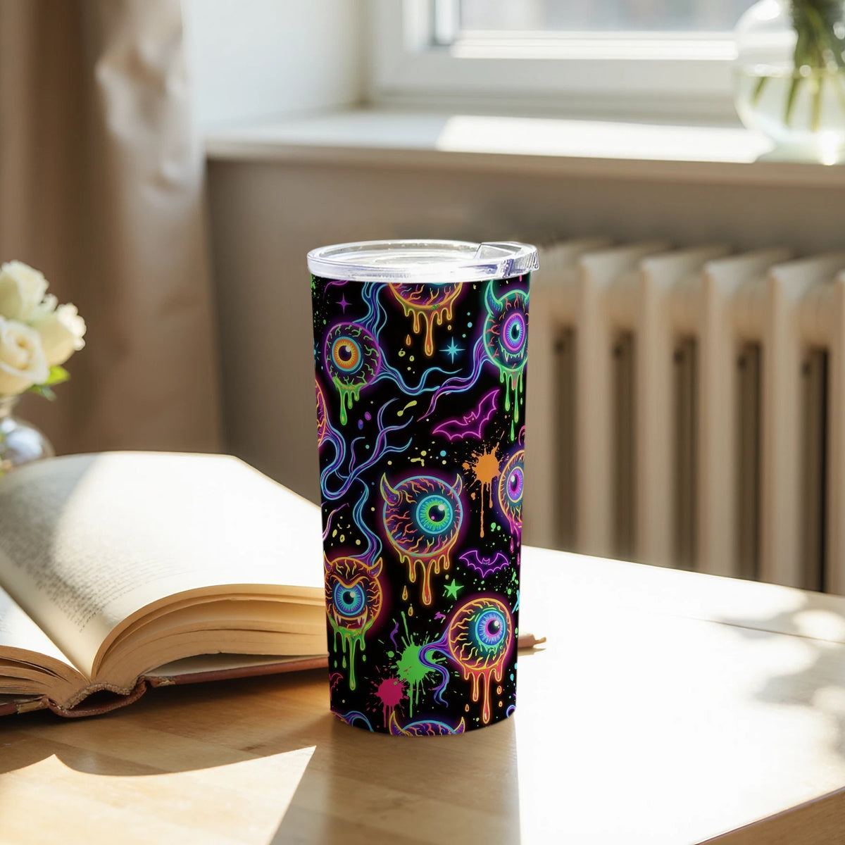 Black tumbler with a neon eyeball and bat pattern and a clear lid.
