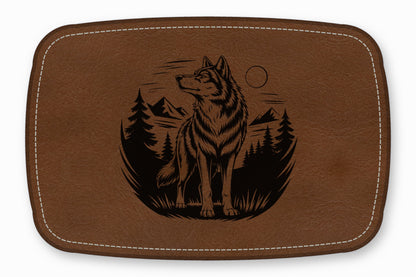 Brown leather patch with rounded corners featuring a black engraved illustration of a wolf, mountains, and trees.