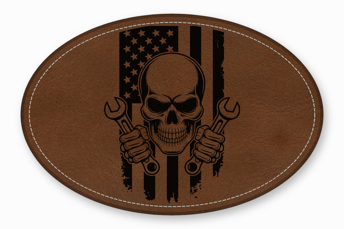 Oval brown leather patch with white stitching featuring a black skull holding two wrenches over an American flag.