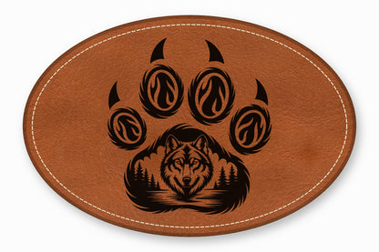 An oval brown leather patch featuring a black laser-engraved wolf face and paw print design.