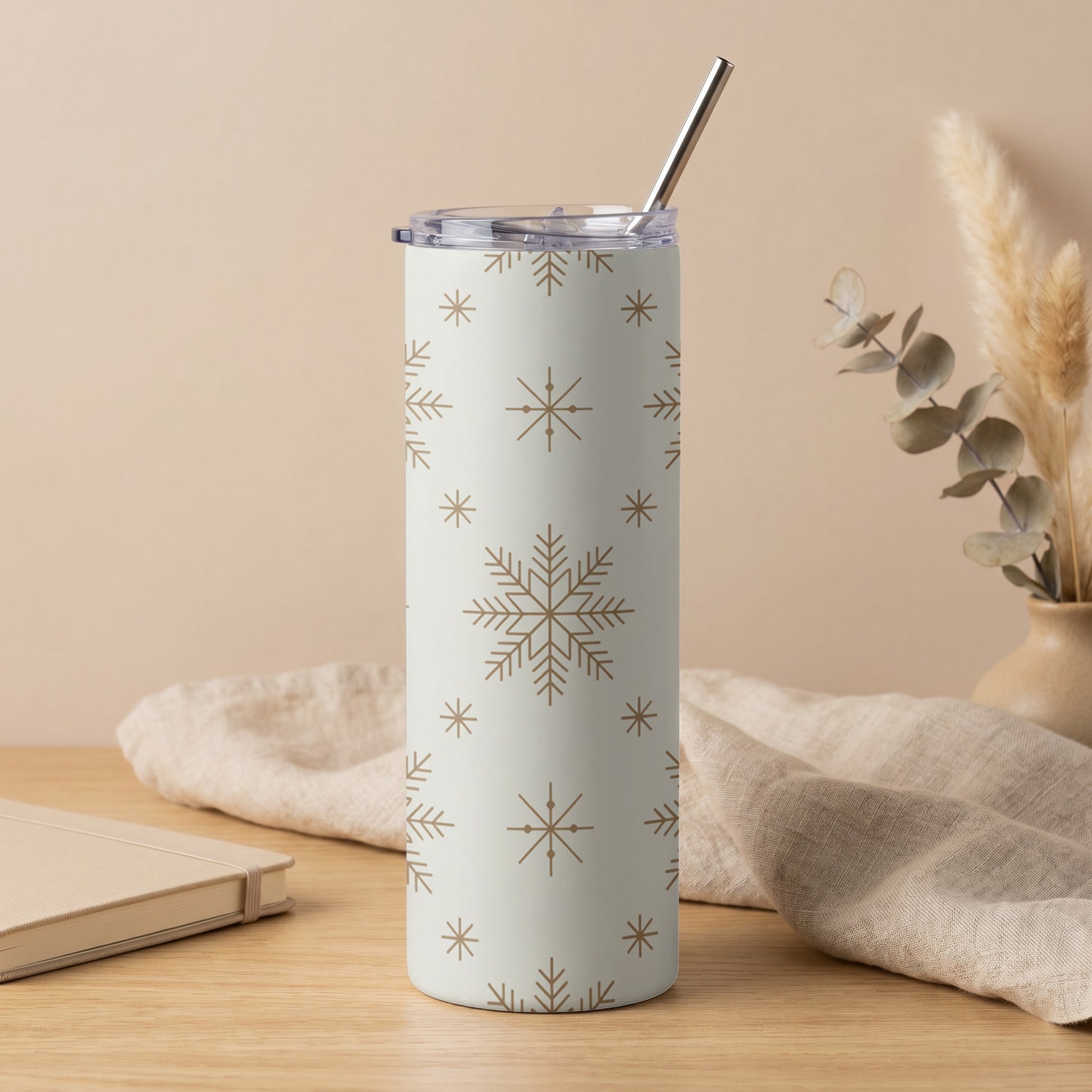 White tumbler with a repeating brown snowflake pattern and metal straw.