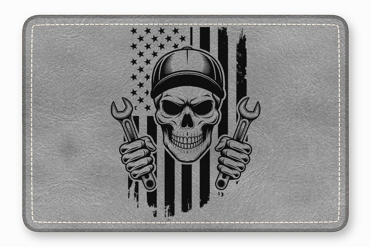 Grey rectangular leather patch featuring a black graphic of a mechanic skull holding wrenches before an American flag.