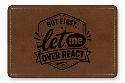 A brown faux leather patch with white stitched borders features black text reading "BUT FIRST... let me OVER REACT".
