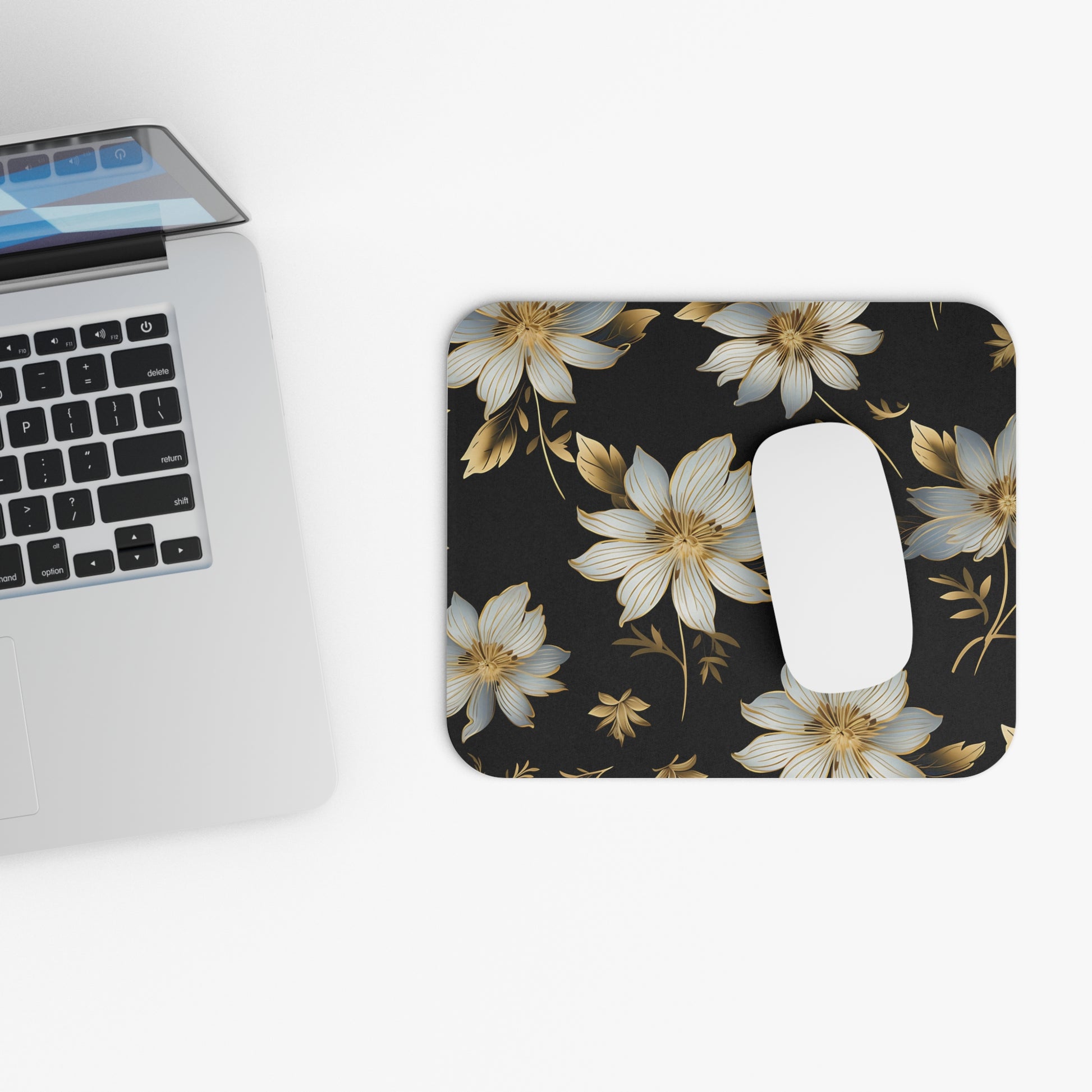 Black mousepad with gold and white floral pattern next to a laptop.