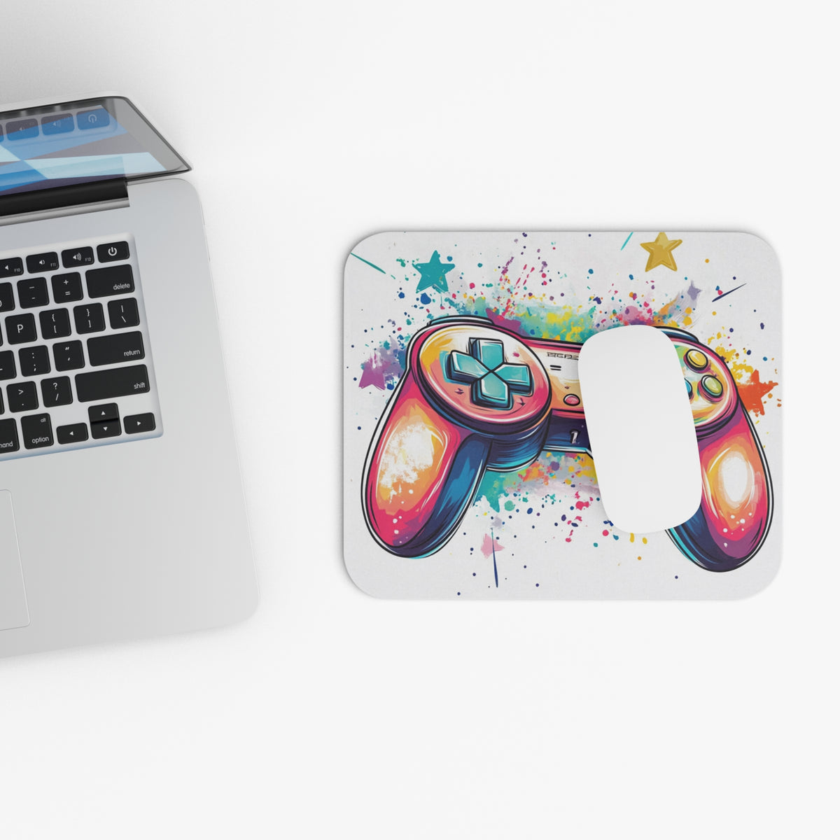 Colorful video game controller art on a white mousepad beside a laptop.