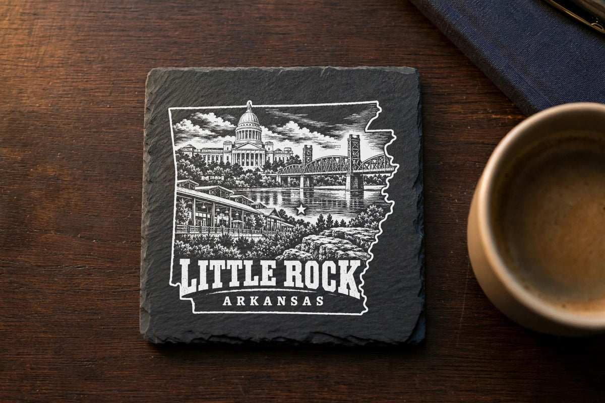 A square slate coaster engraved with a Little Rock, Arkansas skyline outline and city landmarks on a wooden table.