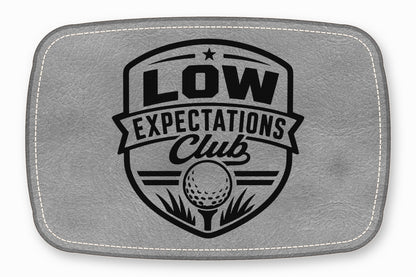 A gray leatherette patch featuring a black golf emblem with the text Low Expectations Club.