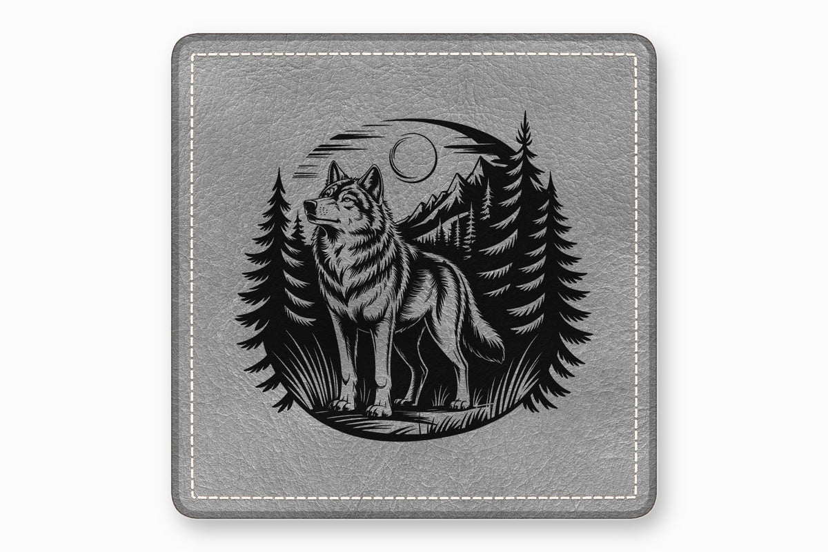 A gray leather coaster featuring a circular black engraved design of a wolf, mountains, and pine trees.