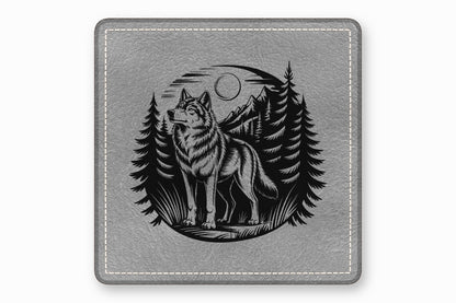 A gray leather coaster featuring a circular black engraved design of a wolf, mountains, and pine trees.