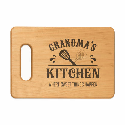 Wooden cutting board with "Grandma's Kitchen Where Sweet Things Happen" text and spatulas.