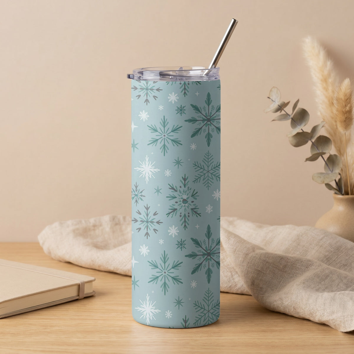 Blue tumbler with white and green snowflake pattern and metal straw.