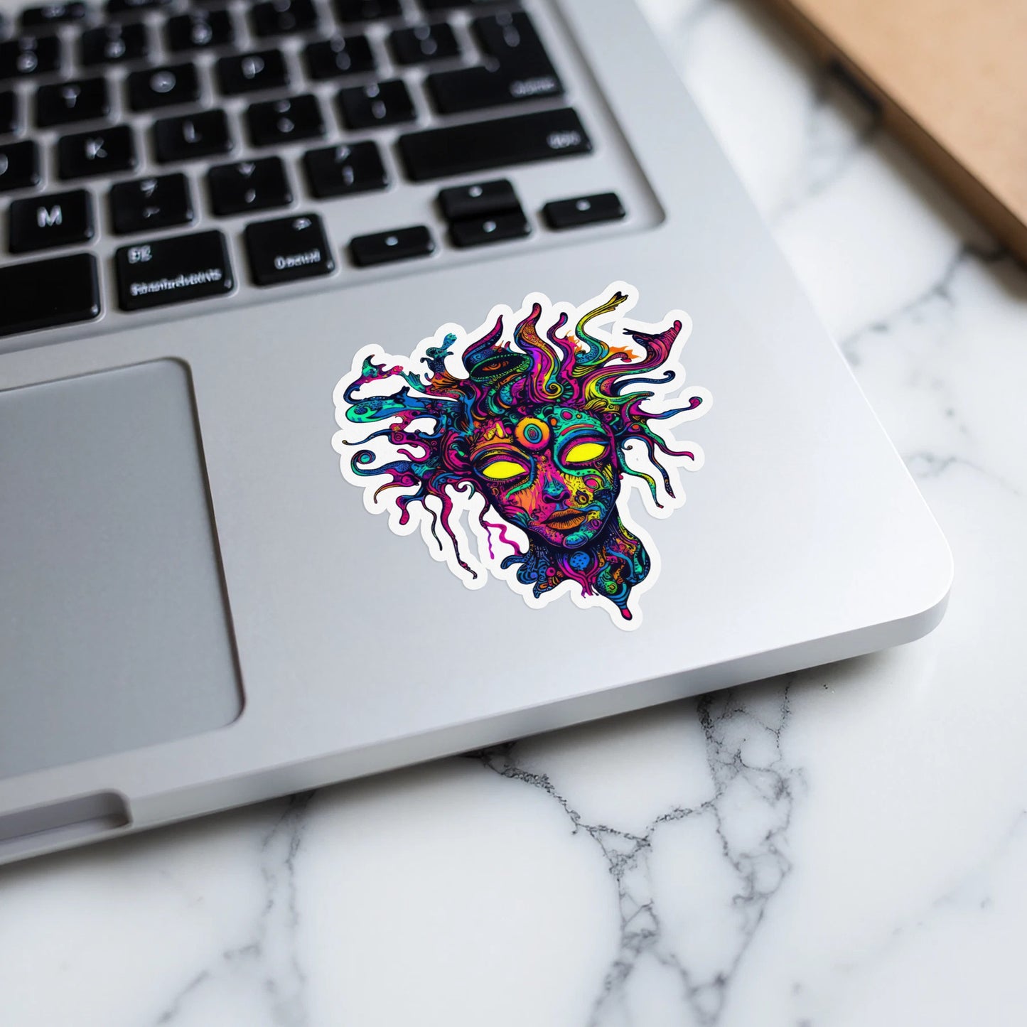Psychedelic face sticker with yellow eyes on a laptop keyboard.