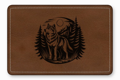 Brown leather rectangular mat with white stitching and a black engraved wolf and forest design.