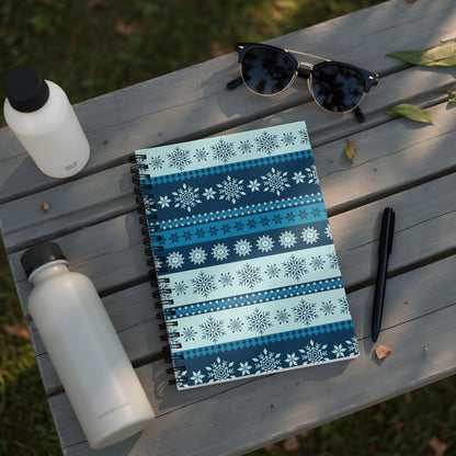 Spiral notebook with blue snowflake pattern, sunglasses, pens, and water bottles on a wooden surface.