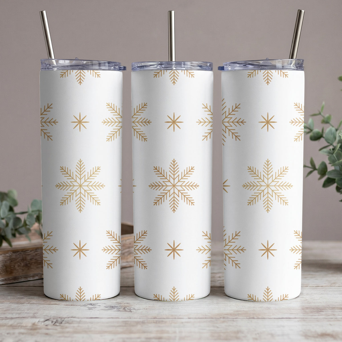 Three white tumblers with gold snowflake pattern and metal straws.