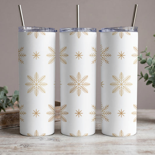 Three white tumblers with gold snowflake pattern and metal straws.