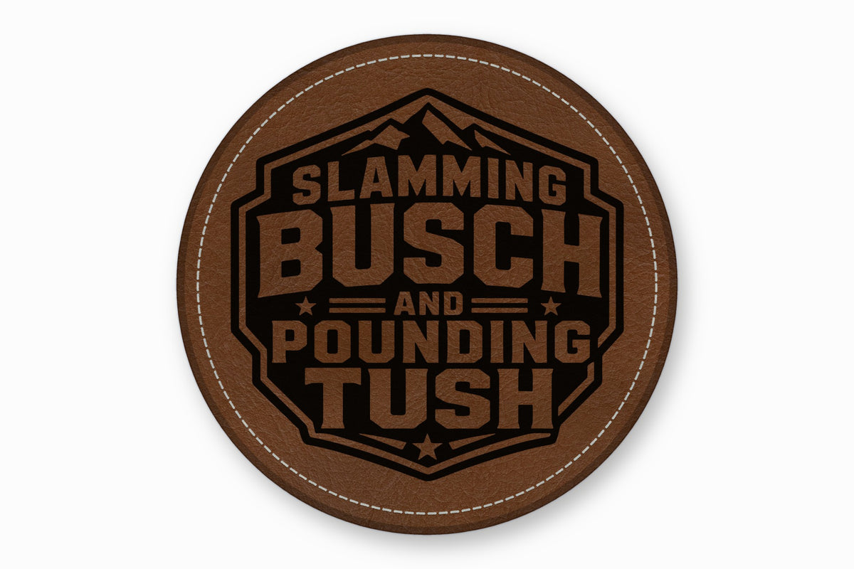 Round brown leatherette patch with white stitching and the engraved text Slamming Busch and Pounding Tush.