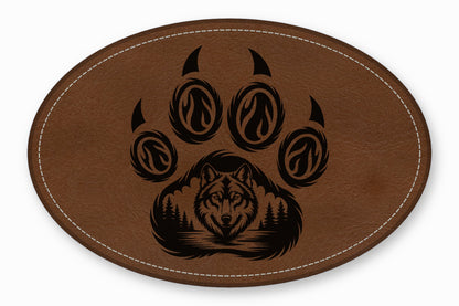 Brown oval leather patch featuring a black laser-engraved wolf face and pine tree paw print design.