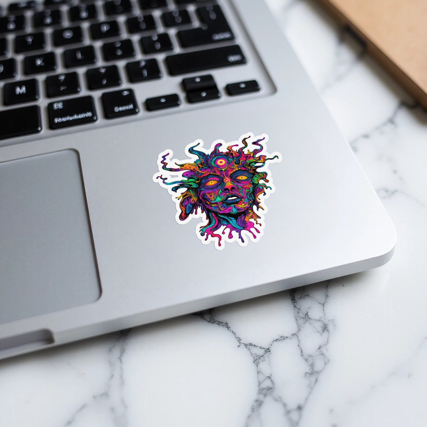 Colorful, psychedelic sticker of a multi-eyed head with swirling hair on a laptop.