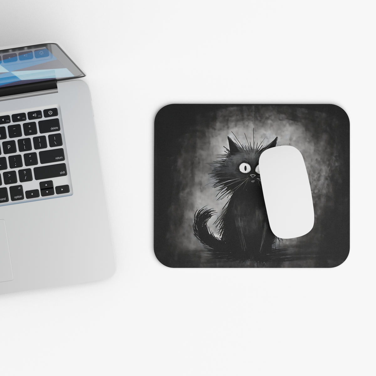 A rectangular black mouse pad featuring a whimsical black cat illustration next to a laptop.