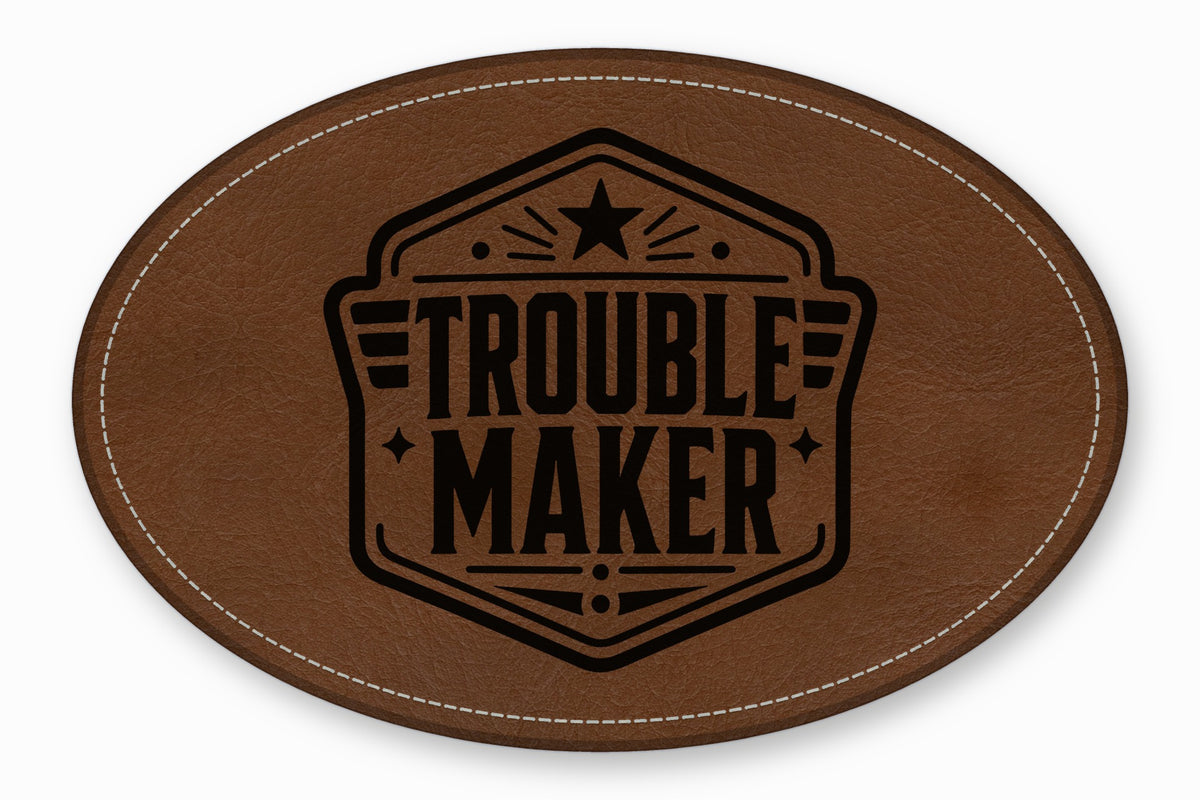 An oval brown leather patch featuring white stitching along the edge and a black printed emblem with the text Trouble Maker.