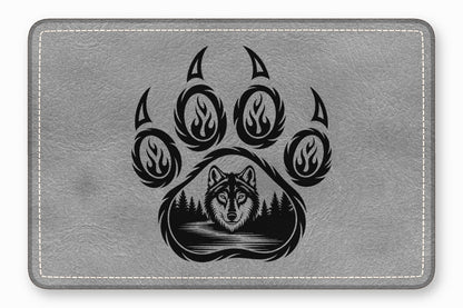 Gray textured leather patch featuring a black bear paw print enclosing a wolf and forest landscape.