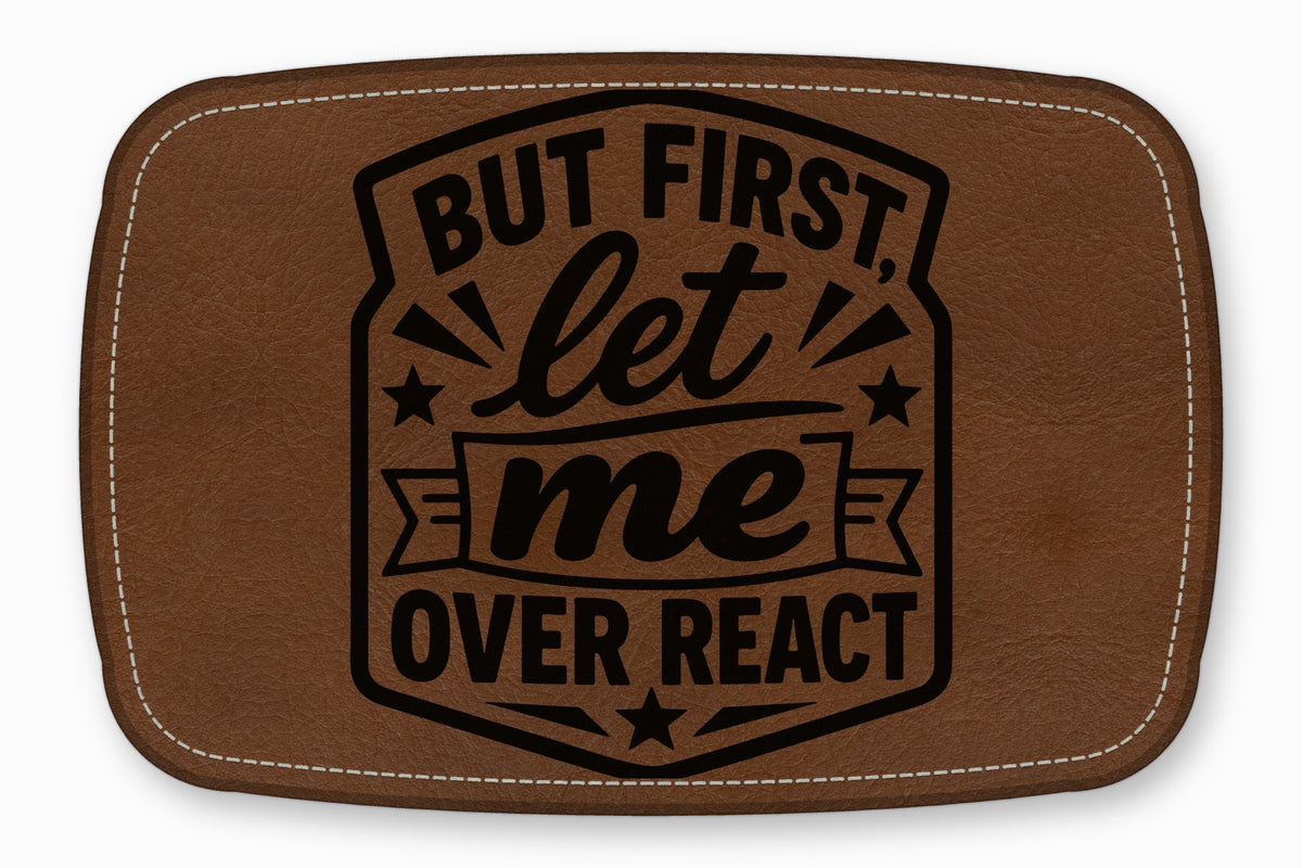 Brown leather patch with rounded corners, white stitching, and black engraved text reading But first, let me overreact.