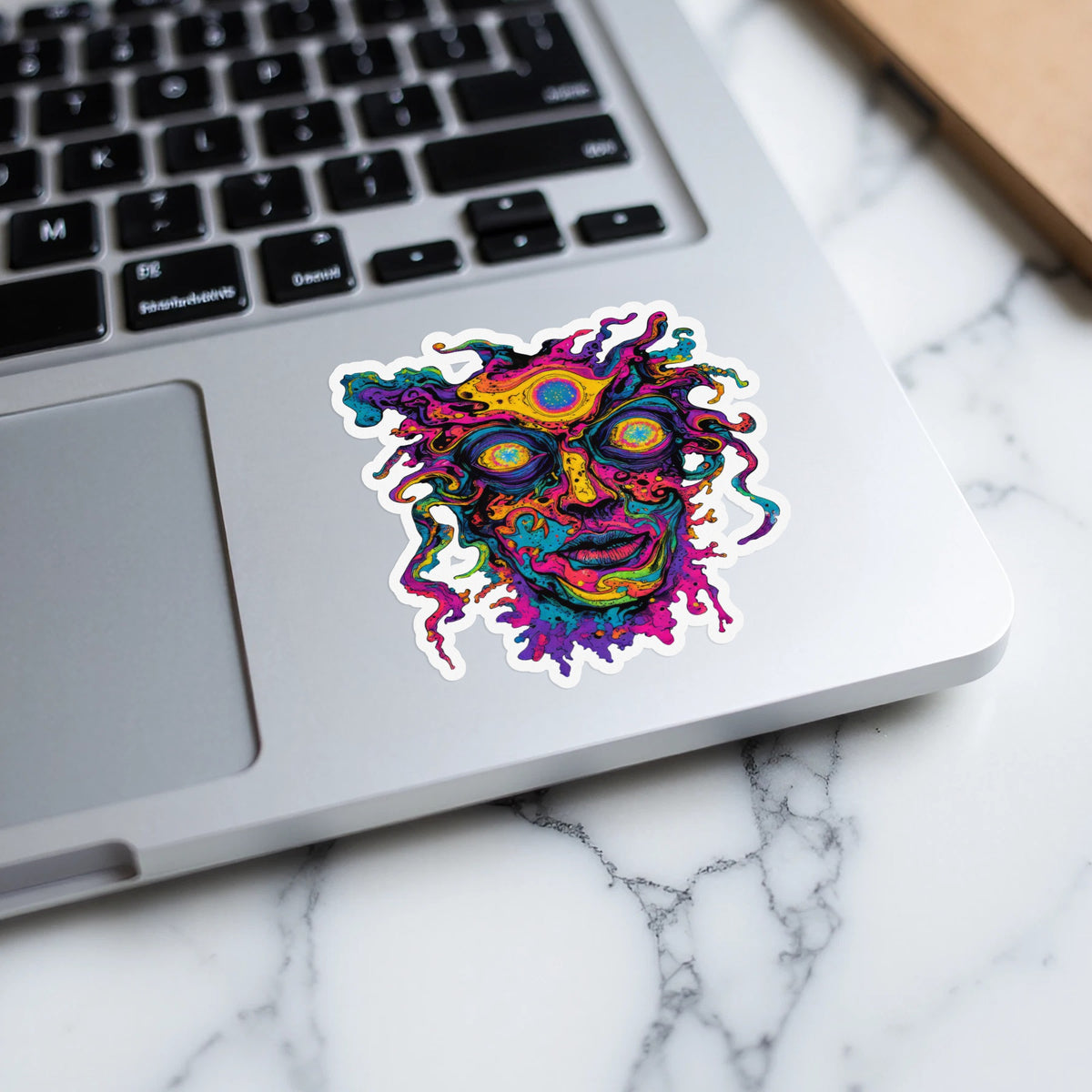 Vibrantly colored abstract face sticker with multiple eyes on a laptop keyboard.