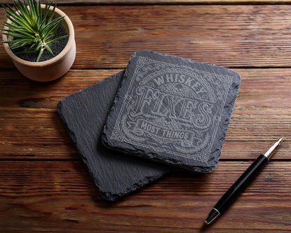 Two slate coasters, one engraved with "Whiskey Fixes Most Things".
