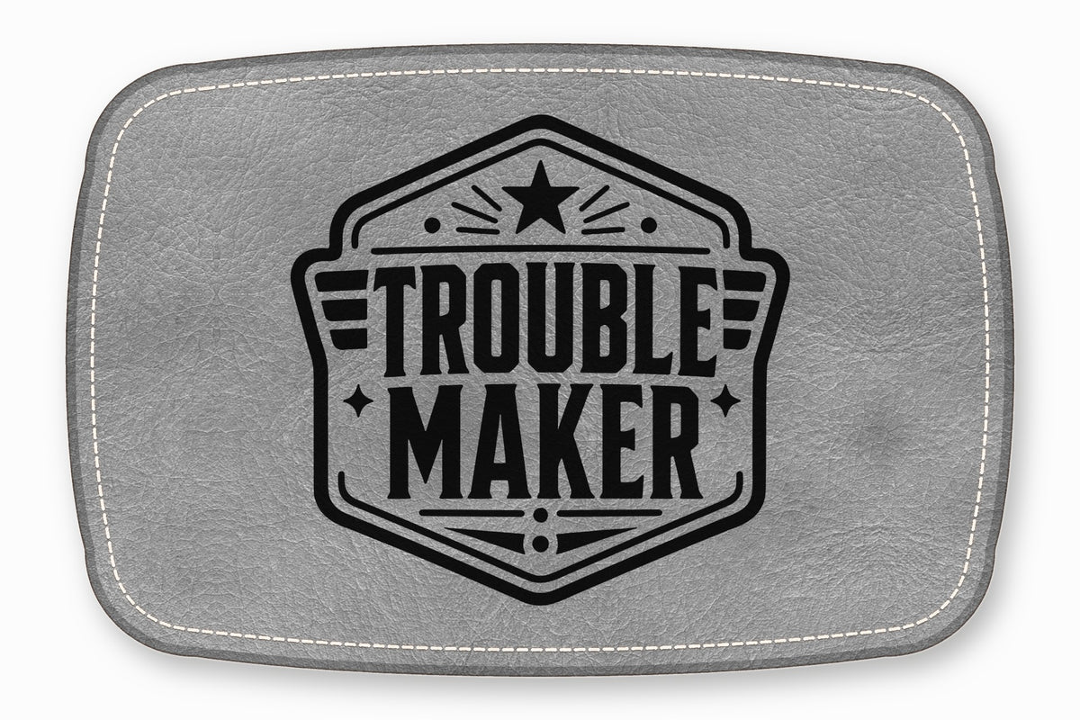 A rectangular grey leather patch with white stitching featuring a black Troublemaker emblem.