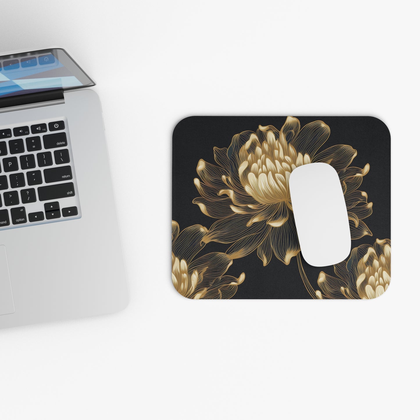 Mousepad with gold line art floral design on black beside a laptop.