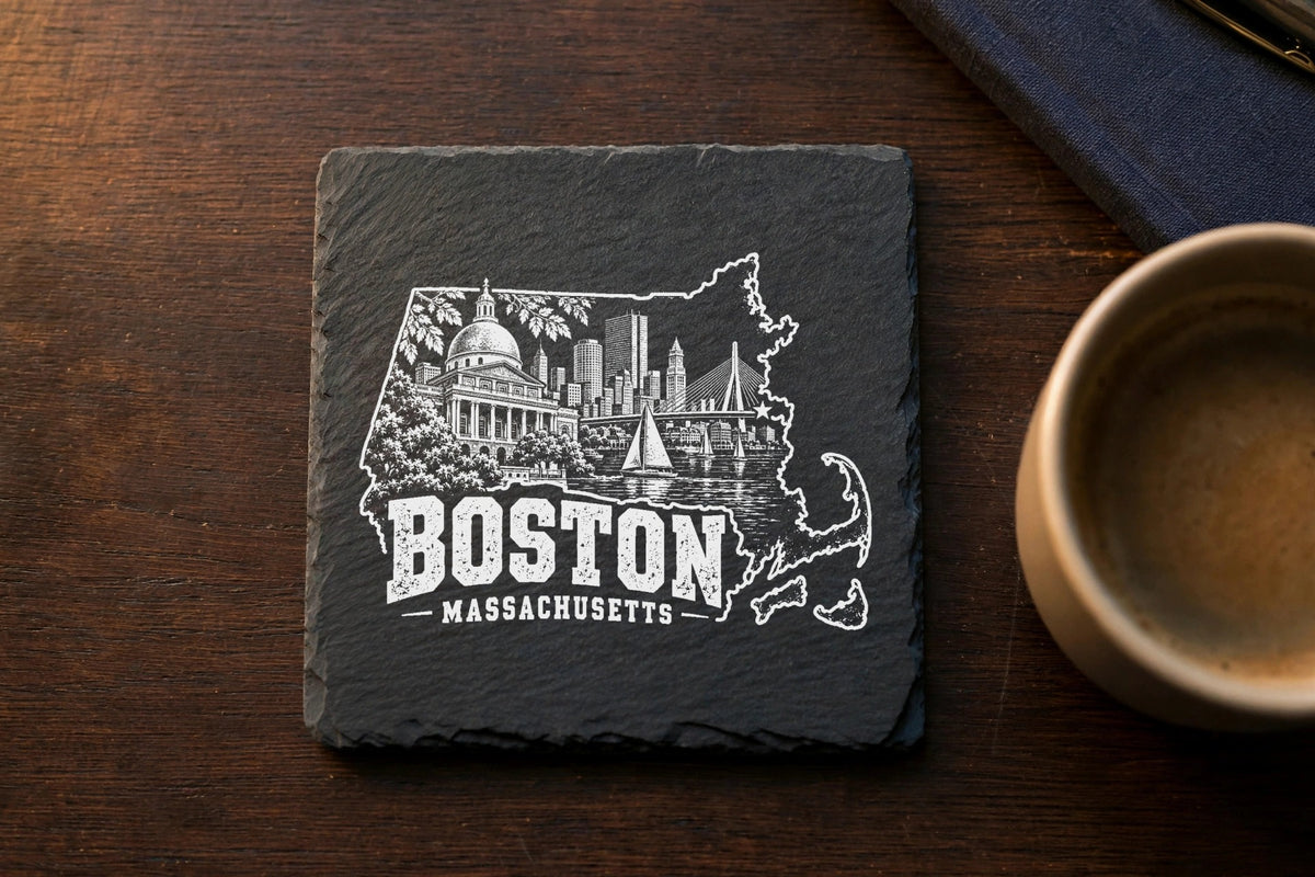 A square slate coaster engraved with a Boston, Massachusetts cityscape inside the state outline on a wooden table.