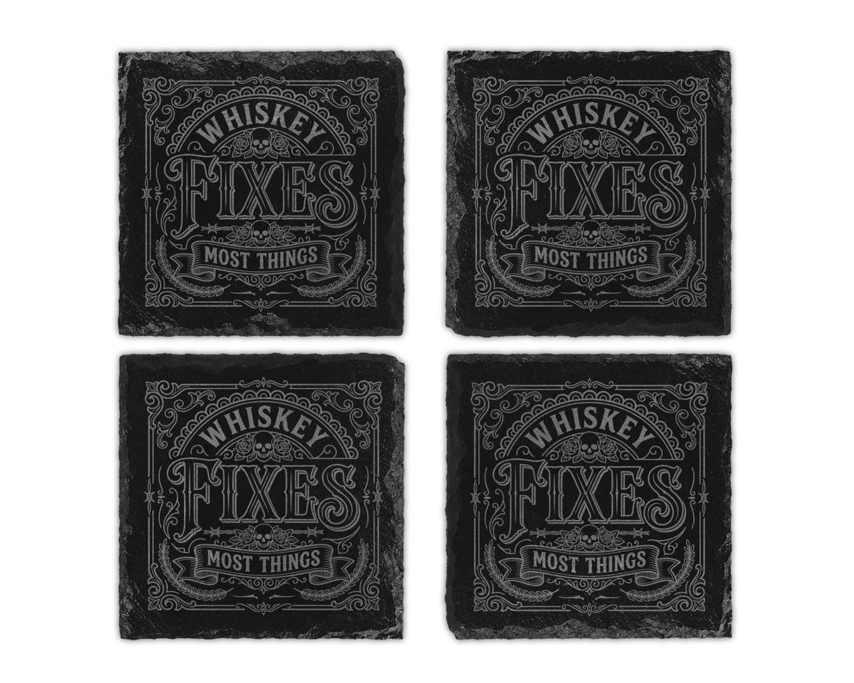 Four black slate coasters with engraved text "WHISKEY FIXES MOST THINGS" and skulls.