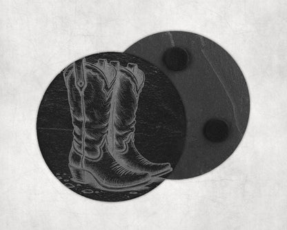 Engraved cowboy boot on a round black slate coaster, another coaster behind it.