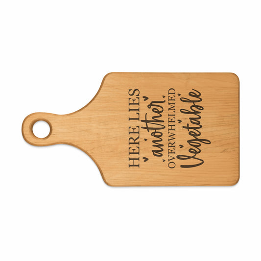 Wooden cutting board with text "HERE LIES another OVERWHELMED Vegetable".