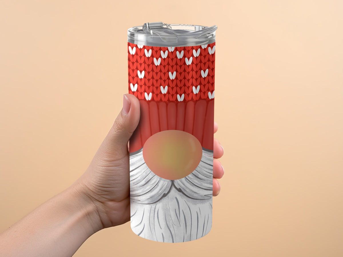 Red tumbler with white hearts and gnome design held against a peach background.