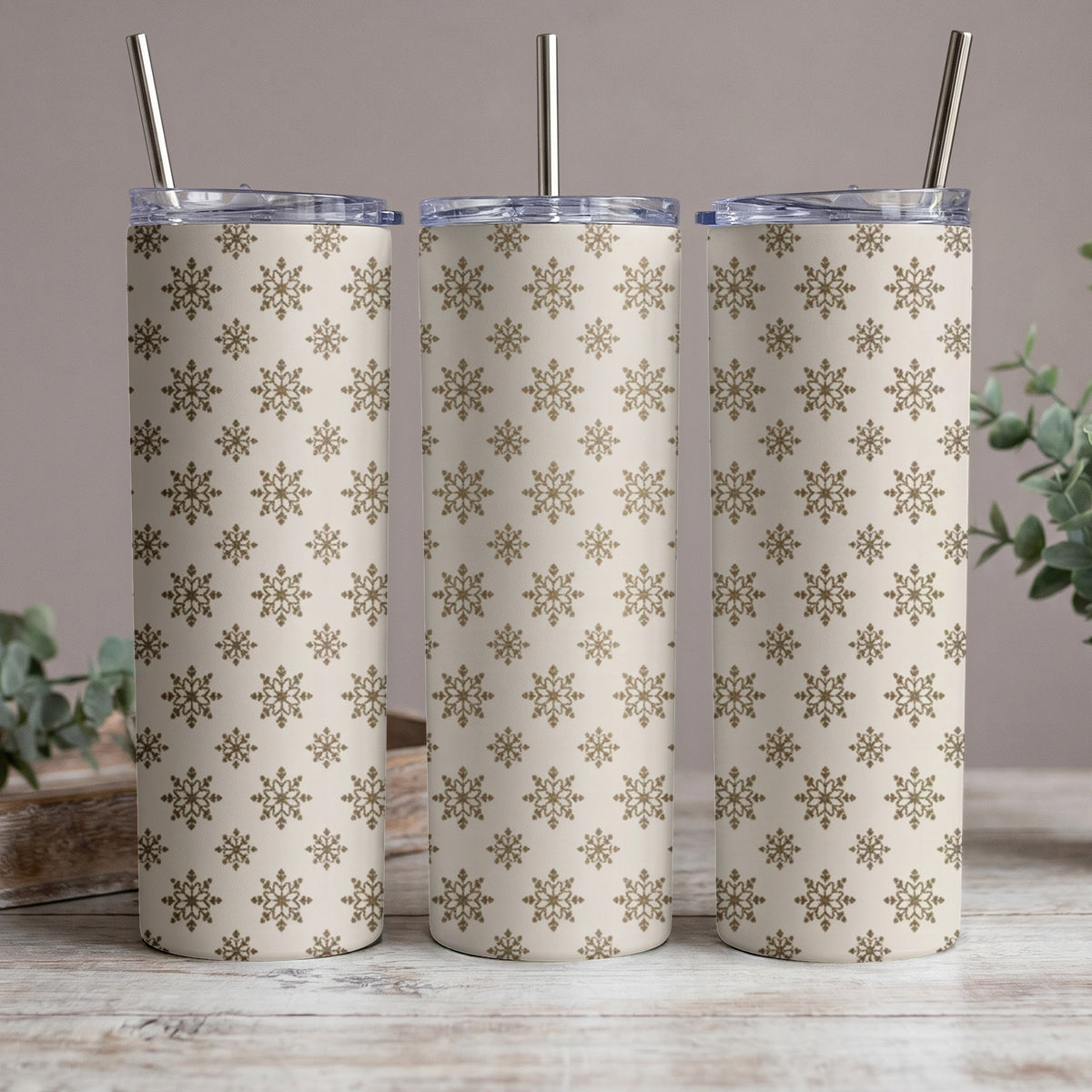 Three tumblers with a beige and gold snowflake pattern and metal straws.