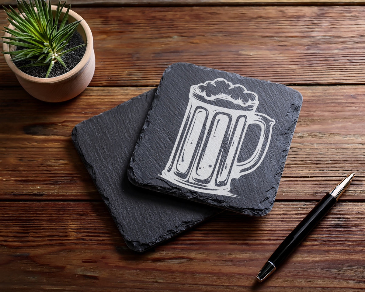 Slate coasters with etched beer mug design on wooden surface.