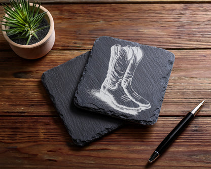 Slate coasters engraved with cowboy boots, next to a plant and pen.