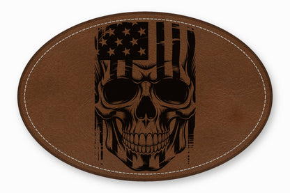 Oval brown leather patch with white stitched border featuring a black engraved American flag skull design.