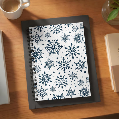 Notebook with dark blue snowflakes on a white background, on a wooden desk.
