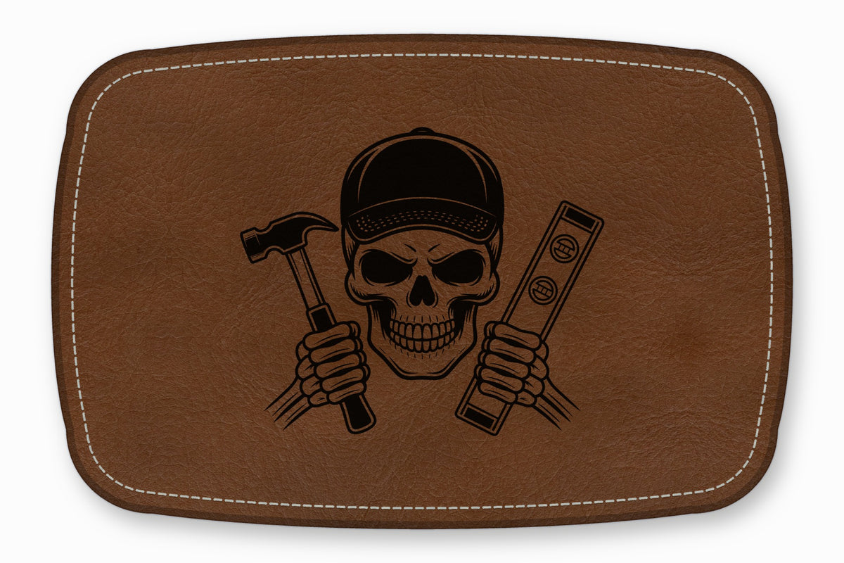 A brown leather patch features an engraved skull wearing a cap while holding a hammer and a level.
