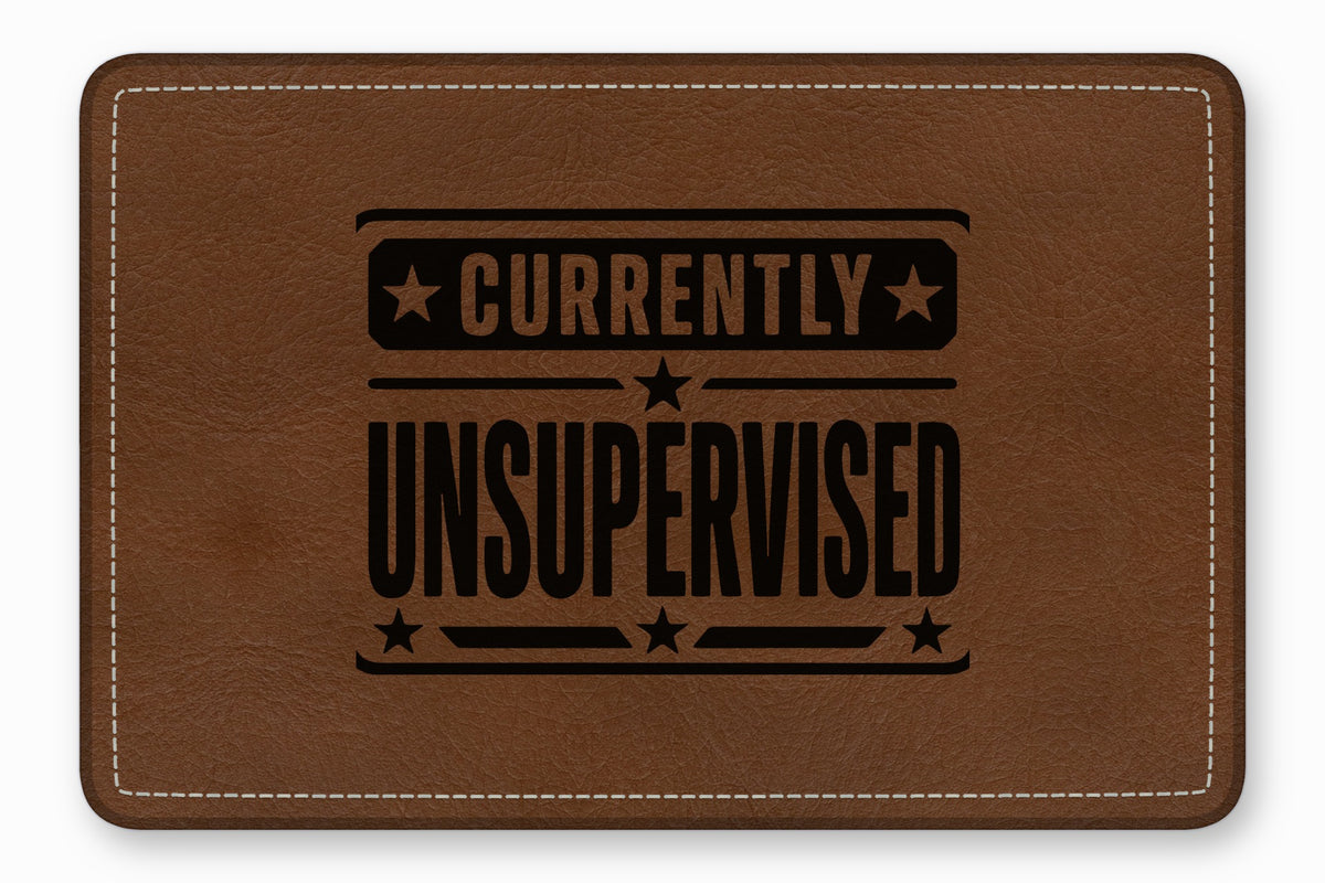 Rectangular brown leather patch with white stitched border and the black text Currently Unsupervised.