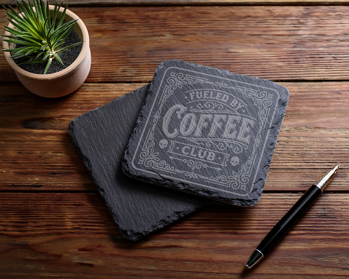 Slate coaster with "Fueled by Coffee Club" etching, plant, and pen.
